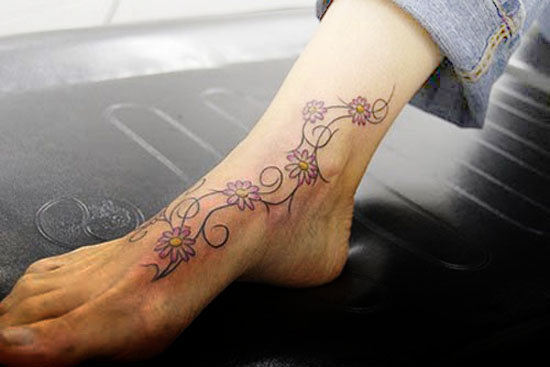 Small flower with vine tattoo design on girl's ankle foot.